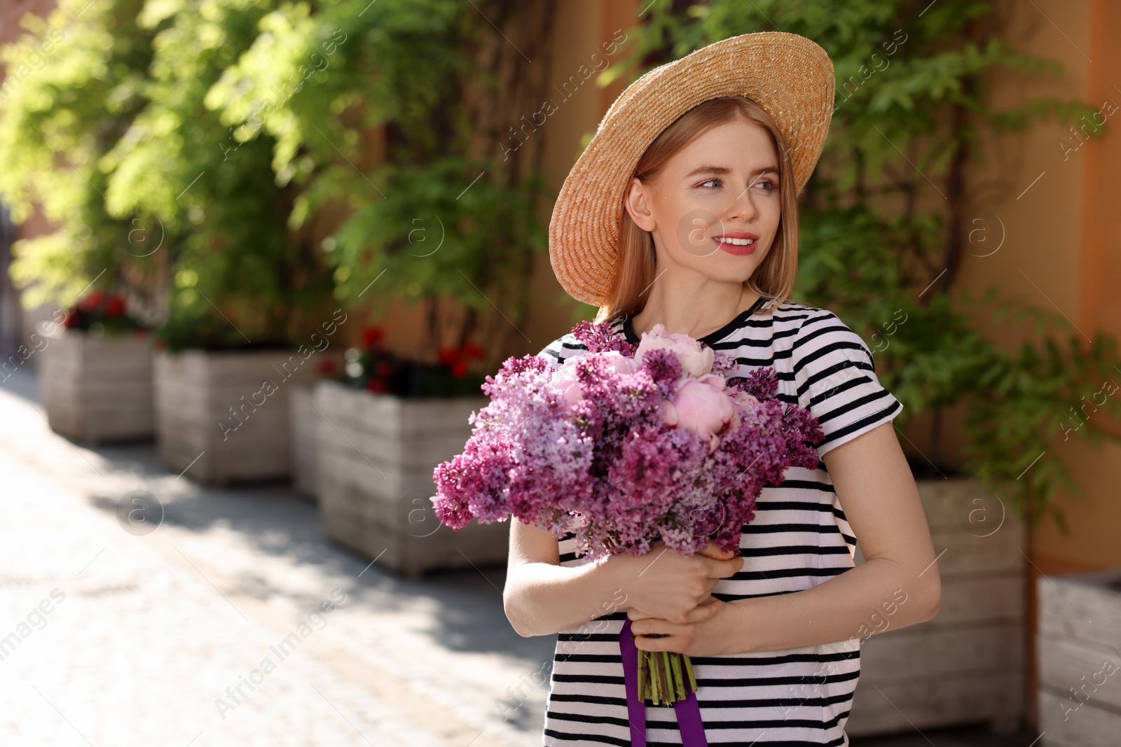 Photo of Beautiful woman with bouquet of spring flowers on city street, space for text