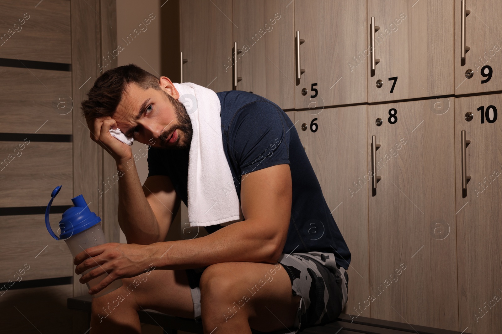 Photo of Handsome tired man with shaker in locker room