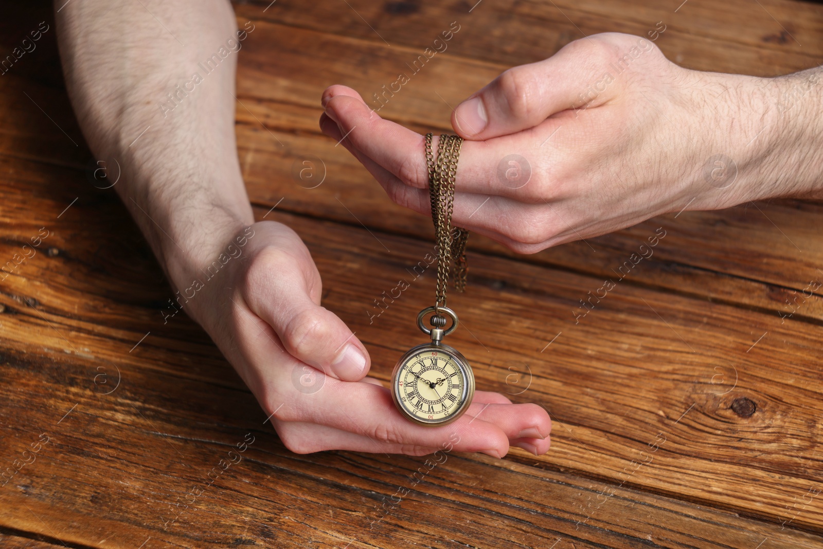 Photo of Man holding chain with elegant pocket watch at wooden table, closeup