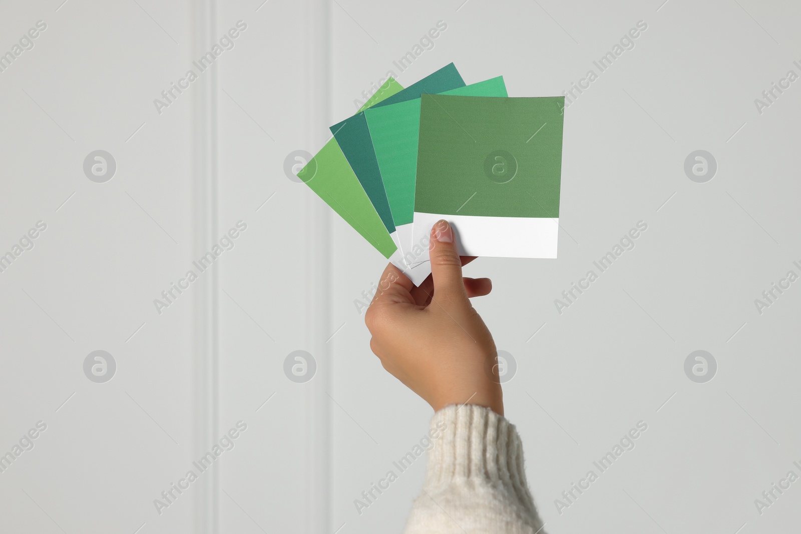 Photo of Woman with color sample cards choosing paint shade for wall indoors, closeup. Interior design