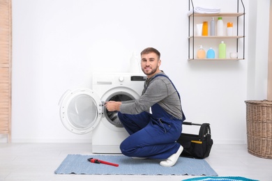 Young plumber fixing washing machine in bathroom