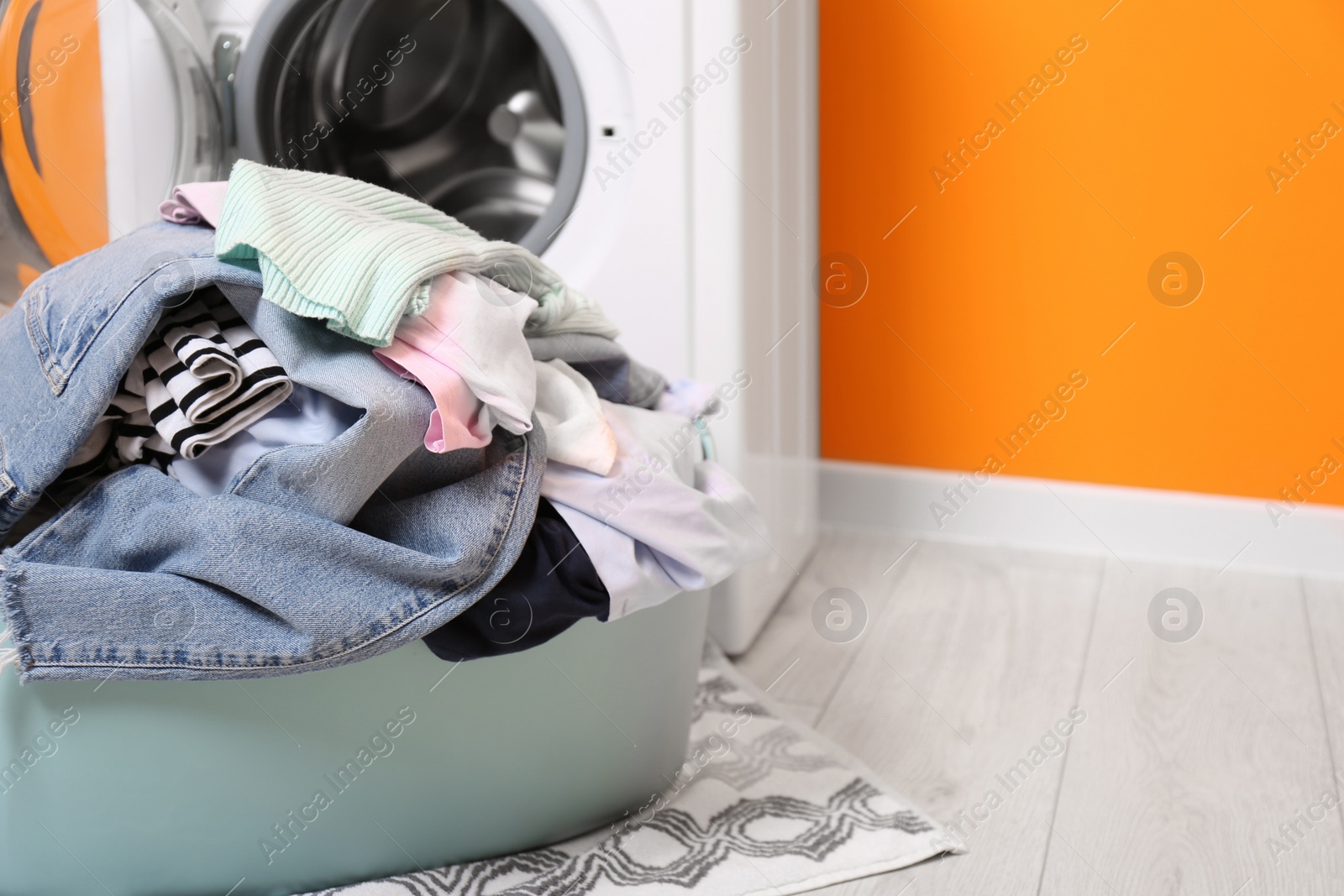 Photo of Laundry basket with clothes on floor near washing machine in bathroom, closeup. Space for text