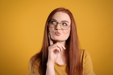 Portrait of thoughtful young woman with gorgeous red hair on yellow background