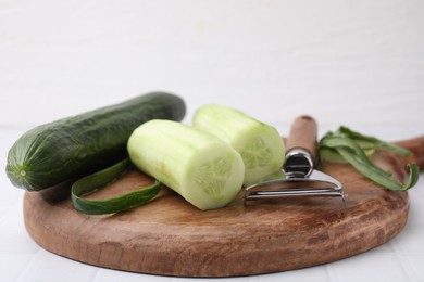 Fresh cucumbers and peeler on white tiled table, closeup