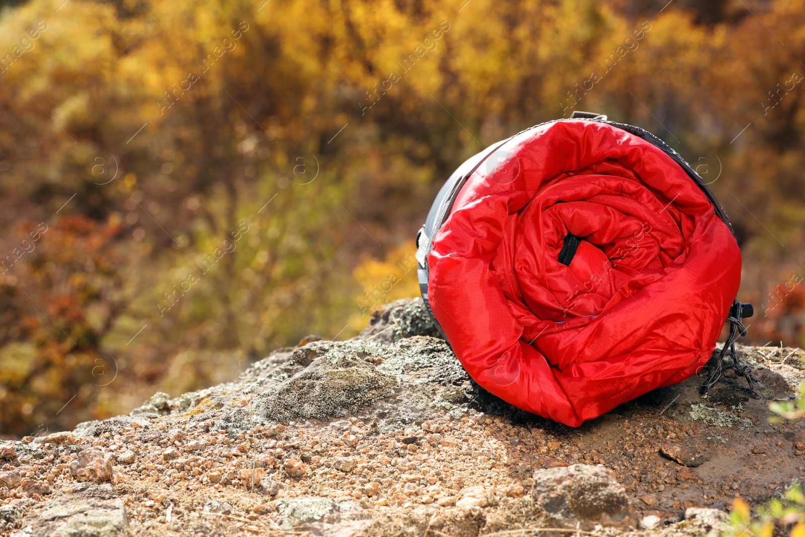 Photo of Red sleeping bag on rock outdoors, space for text. Camping equipment