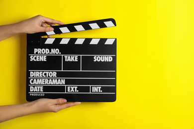 Photo of Woman holding clapperboard on yellow background, closeup with space for text. Cinema production
