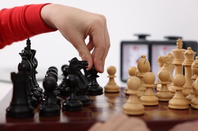 Photo of Little child playing chess at table indoors, closeup