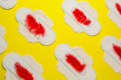 Photo of Menstrual pads with red feathers on yellow background, flat lay