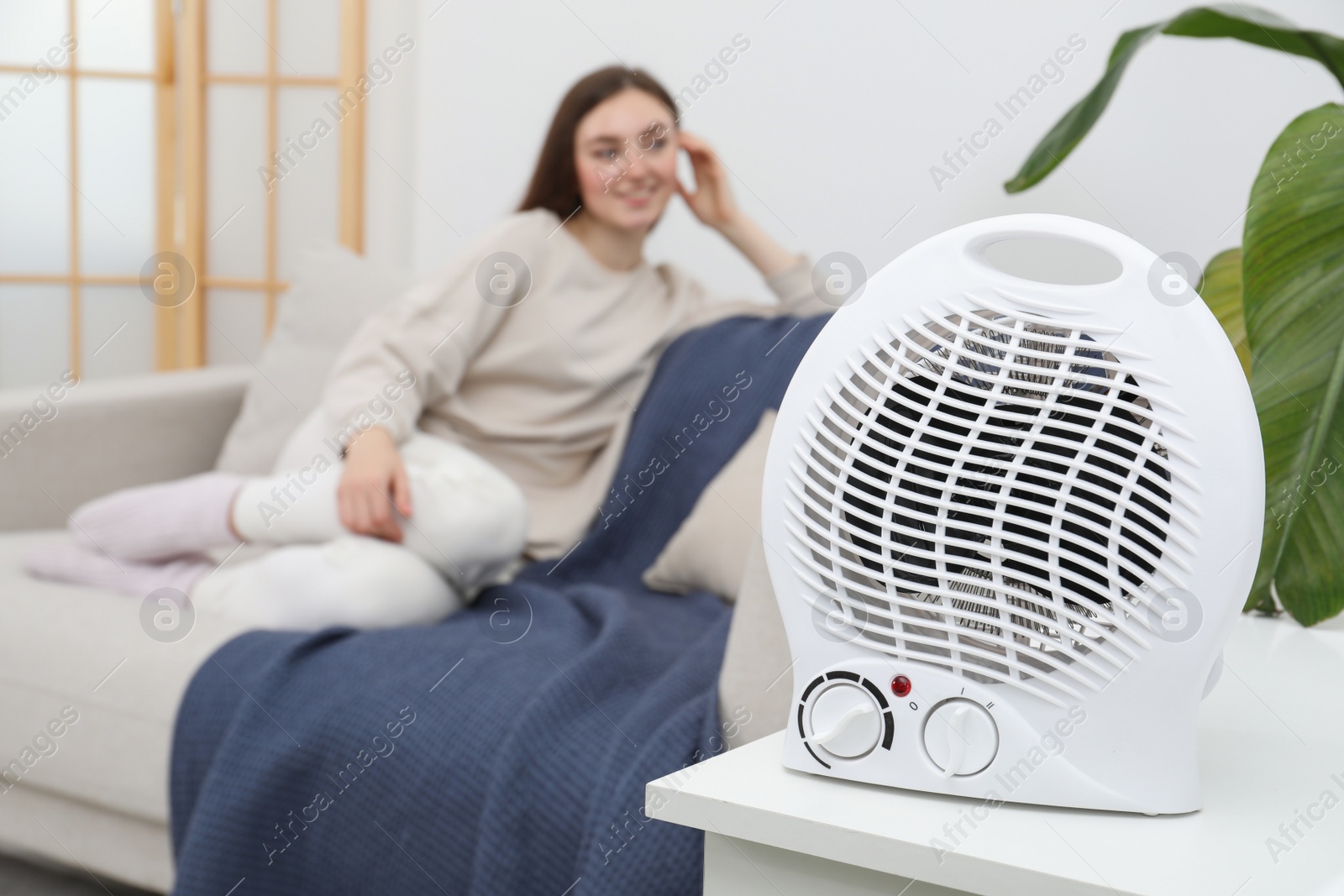 Photo of Woman sitting in room, focus on electric fan heater