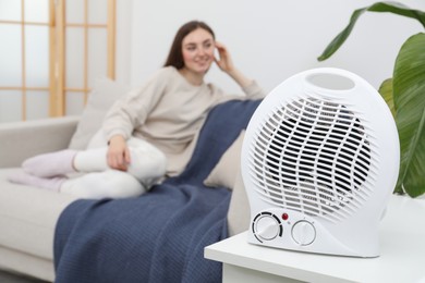Photo of Woman sitting in room, focus on electric fan heater