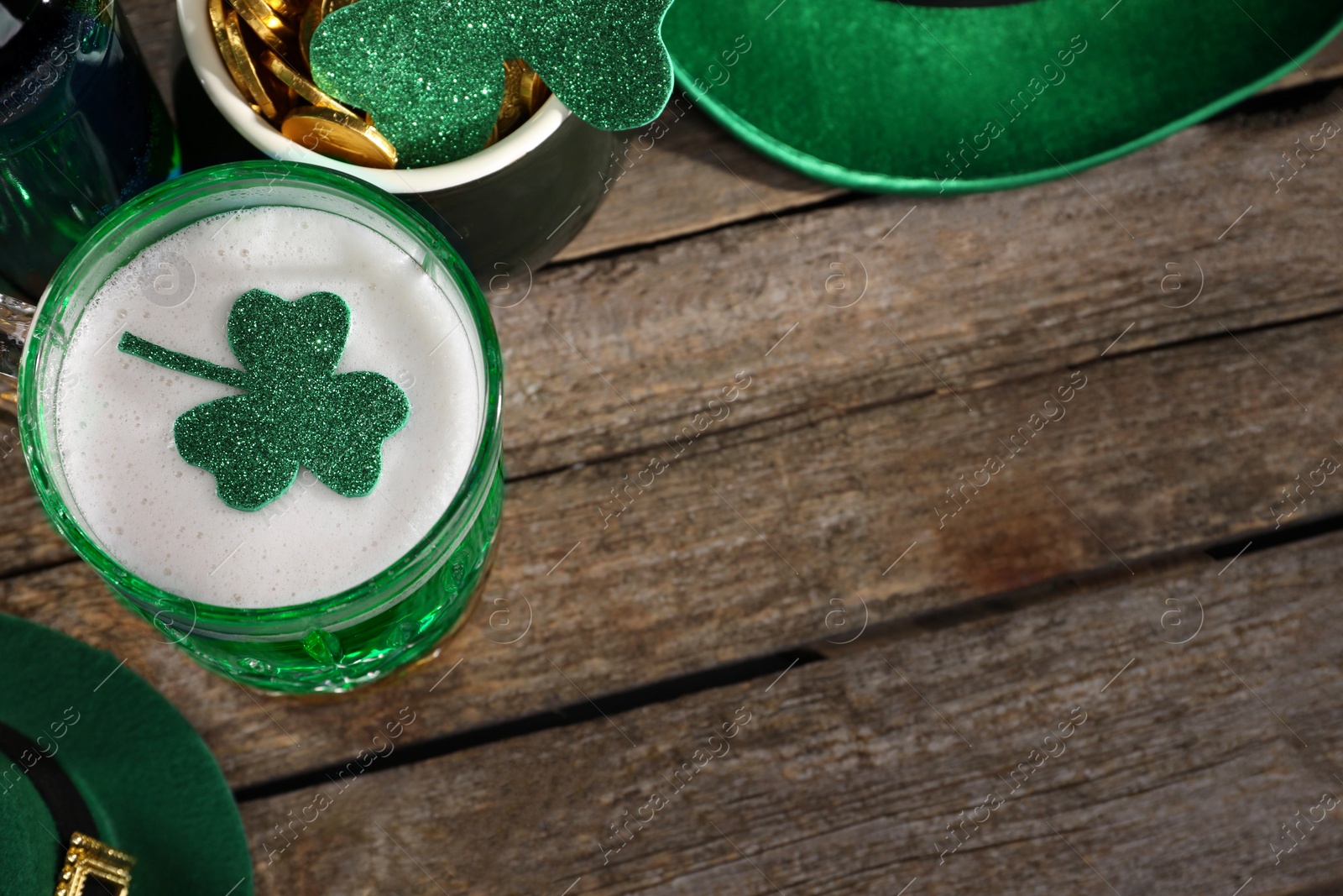 Photo of St. Patrick's day party. Green beer, leprechaun hat, pot of gold and decorative clover leaves on wooden table, above view. Space for text