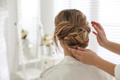 Photo of Professional stylist making wedding hairstyle for bride in salon, back view