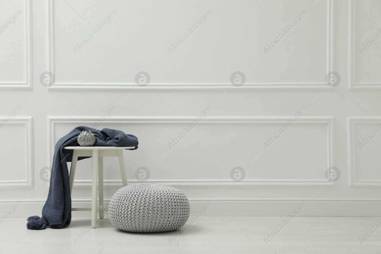 Photo of Knitted pouf near table with plaid and elegant candle holder indoors. Space for text