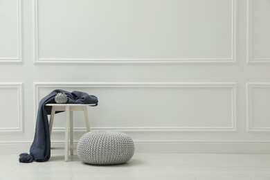 Photo of Knitted pouf near table with plaid and elegant candle holder indoors. Space for text