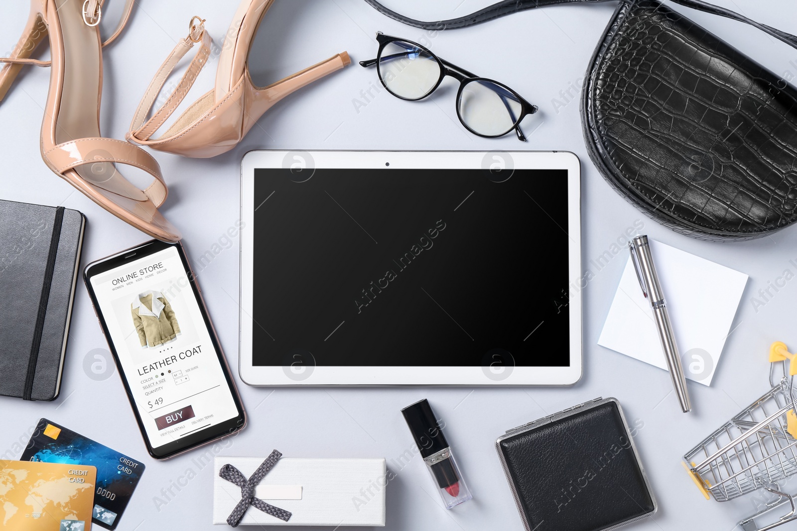 Photo of Online store. Tablet, smartphone, stationery, credit cards, shopping cart and accessories on light grey background, flat lay
