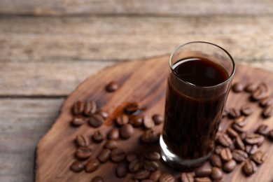 Glass of coffee liqueur and beans on wooden table, closeup. Space for text