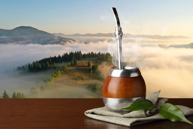 Image of Calabash with mate tea and bombilla on wooden table and beautiful view of mountain landscape, space for text