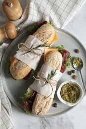 Photo of Delicious sandwiches with bresaola, cheese and lettuce served on white marble table, flat lay