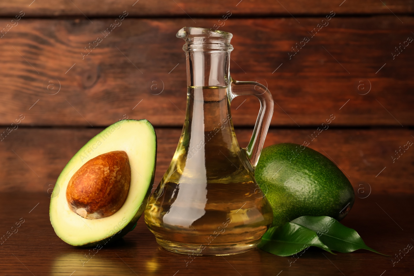 Photo of Glass jug of cooking oil and fresh avocados on wooden table