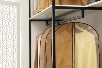 Photo of Garment bags with clothes on rack in dressing room. Space for text