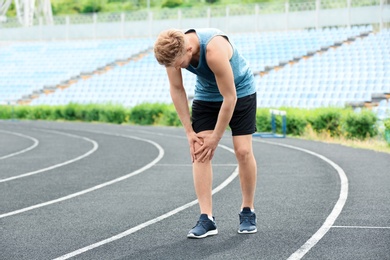 Photo of Man in sportswear suffering from knee pain at stadium