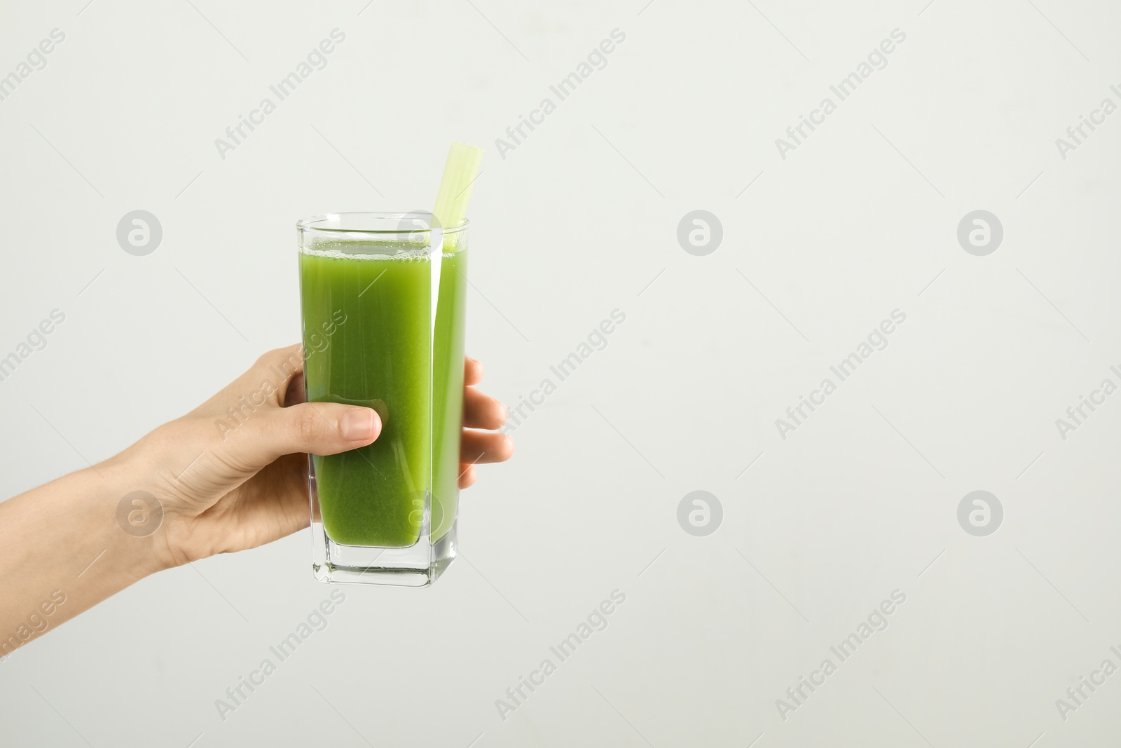 Photo of Woman holding glass of delicious celery juice on light grey background, closeup. Space for text