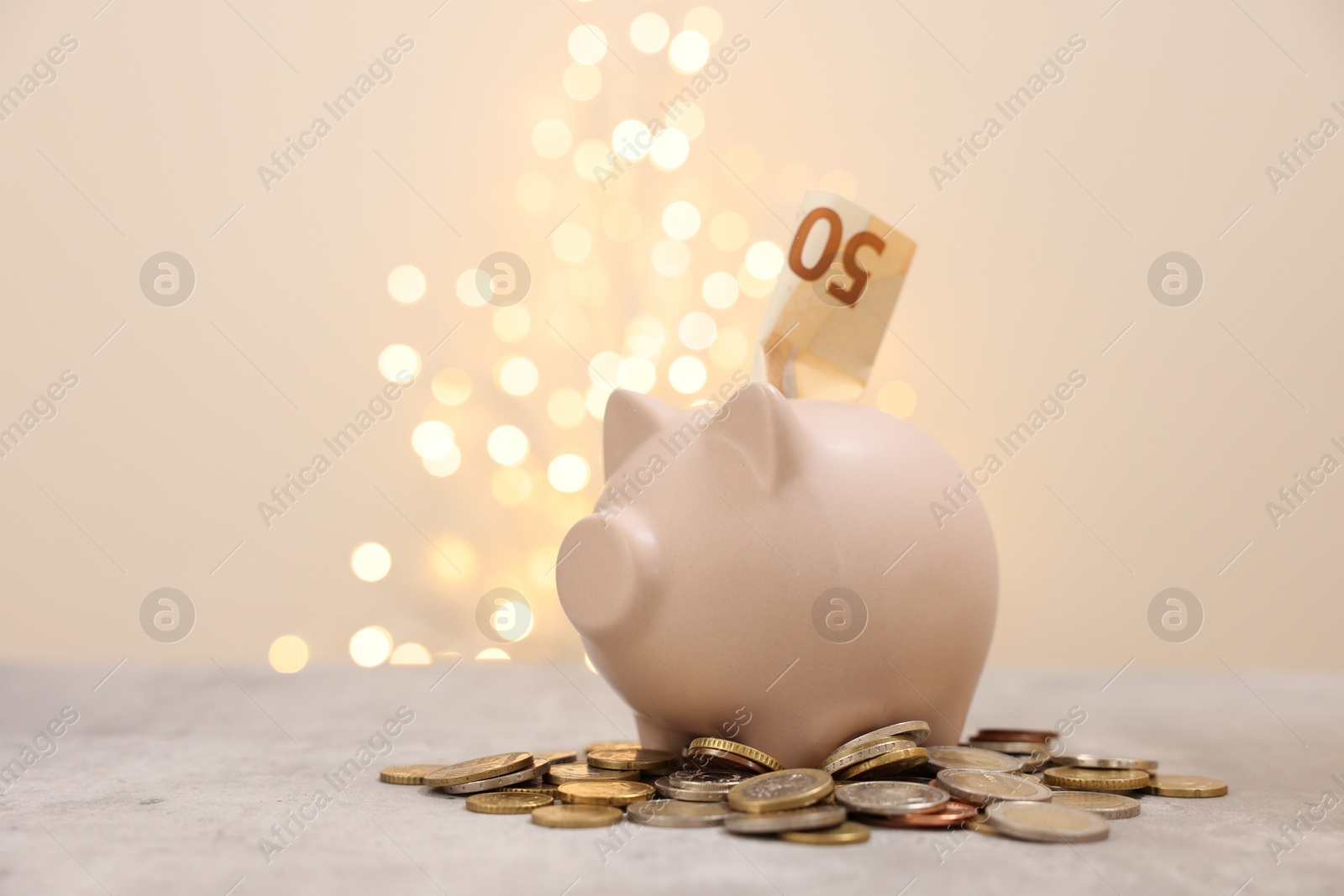 Photo of Piggy bank with euro banknote and coins on grey table against blurred lights, space for text