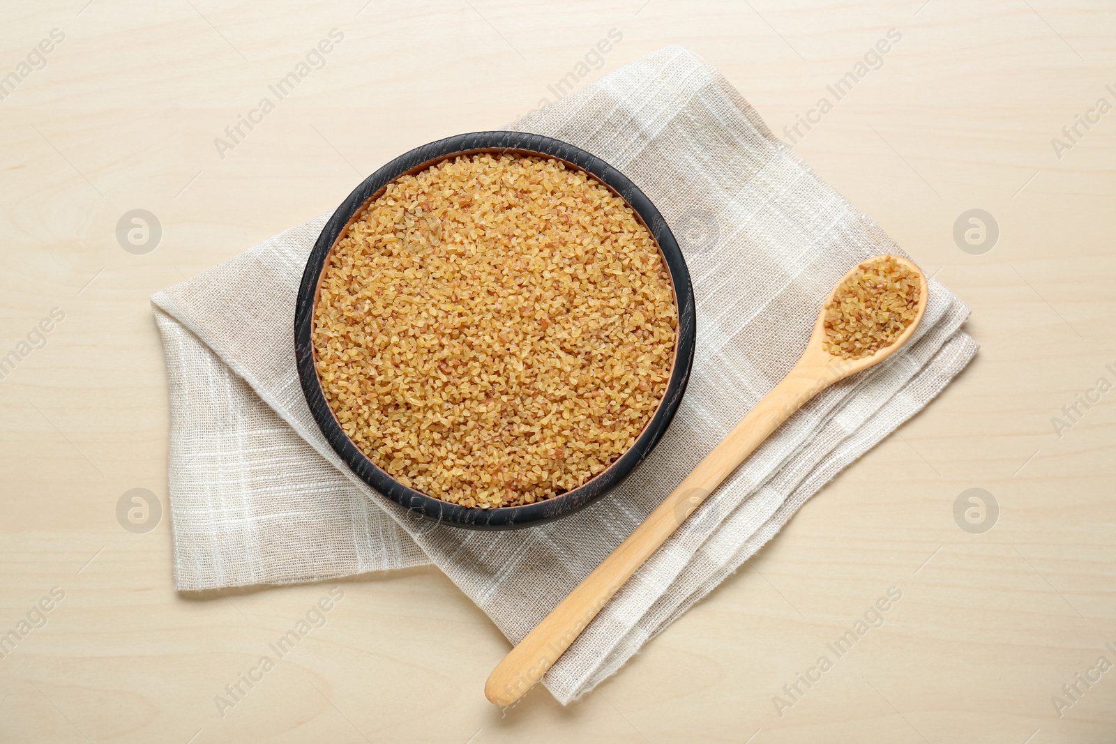 Photo of Bowl and spoon with uncooked bulgur on wooden table, flat lay