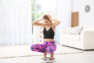 Sad young woman measuring her weight using scales on floor at home. Weight loss motivation