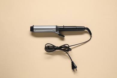 Curling iron on beige background, top view