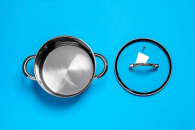 Empty steel pot and lid on light blue background, flat lay