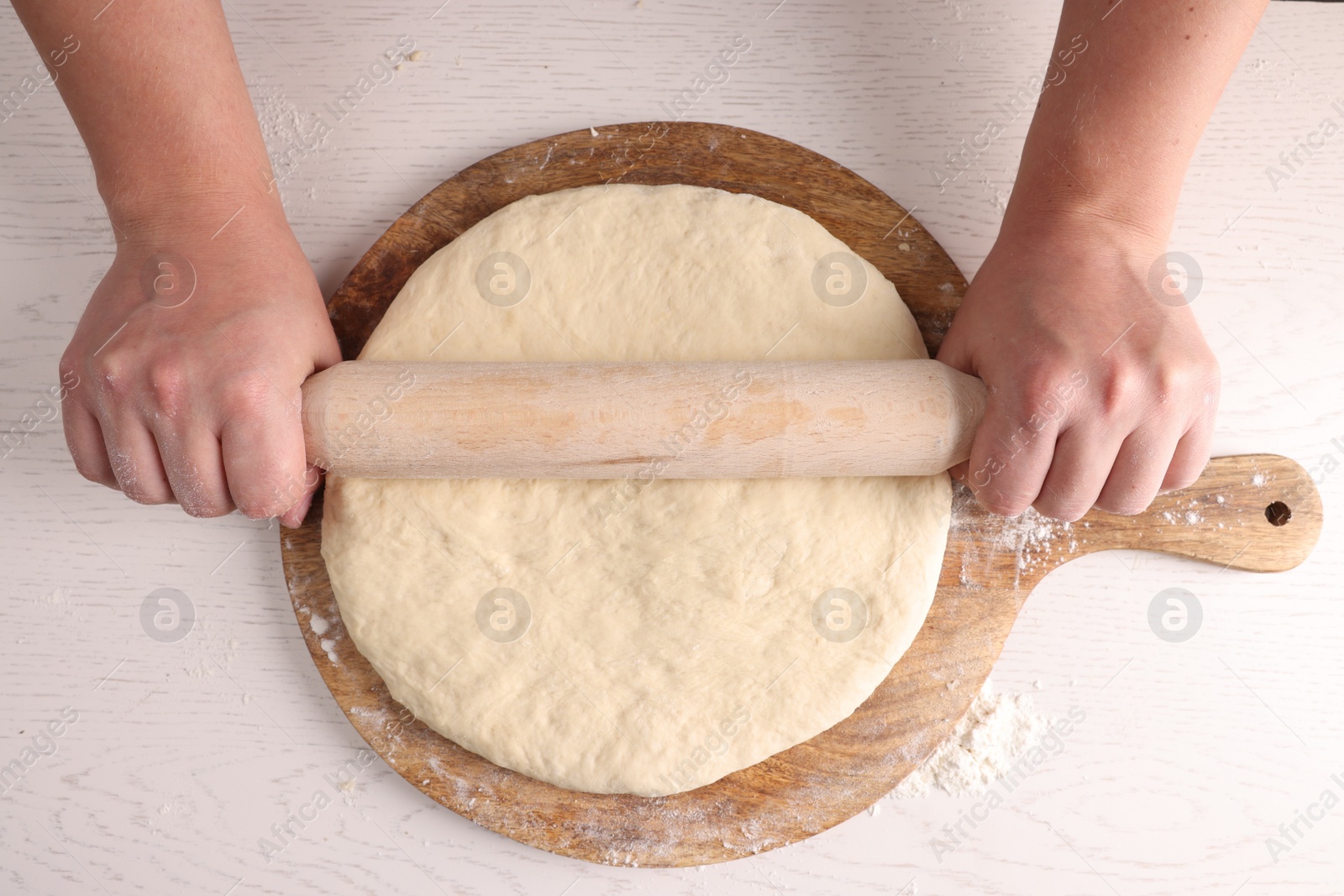 Photo of Man rolling dough with wooden pin at white table, top view