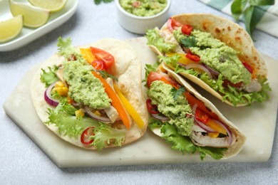 Photo of Delicious tacos with guacamole, meat and vegetables on light grey table, closeup