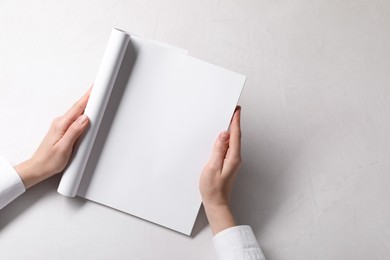 Woman holding notebook with blank pages at white table, top view. Mockup for design