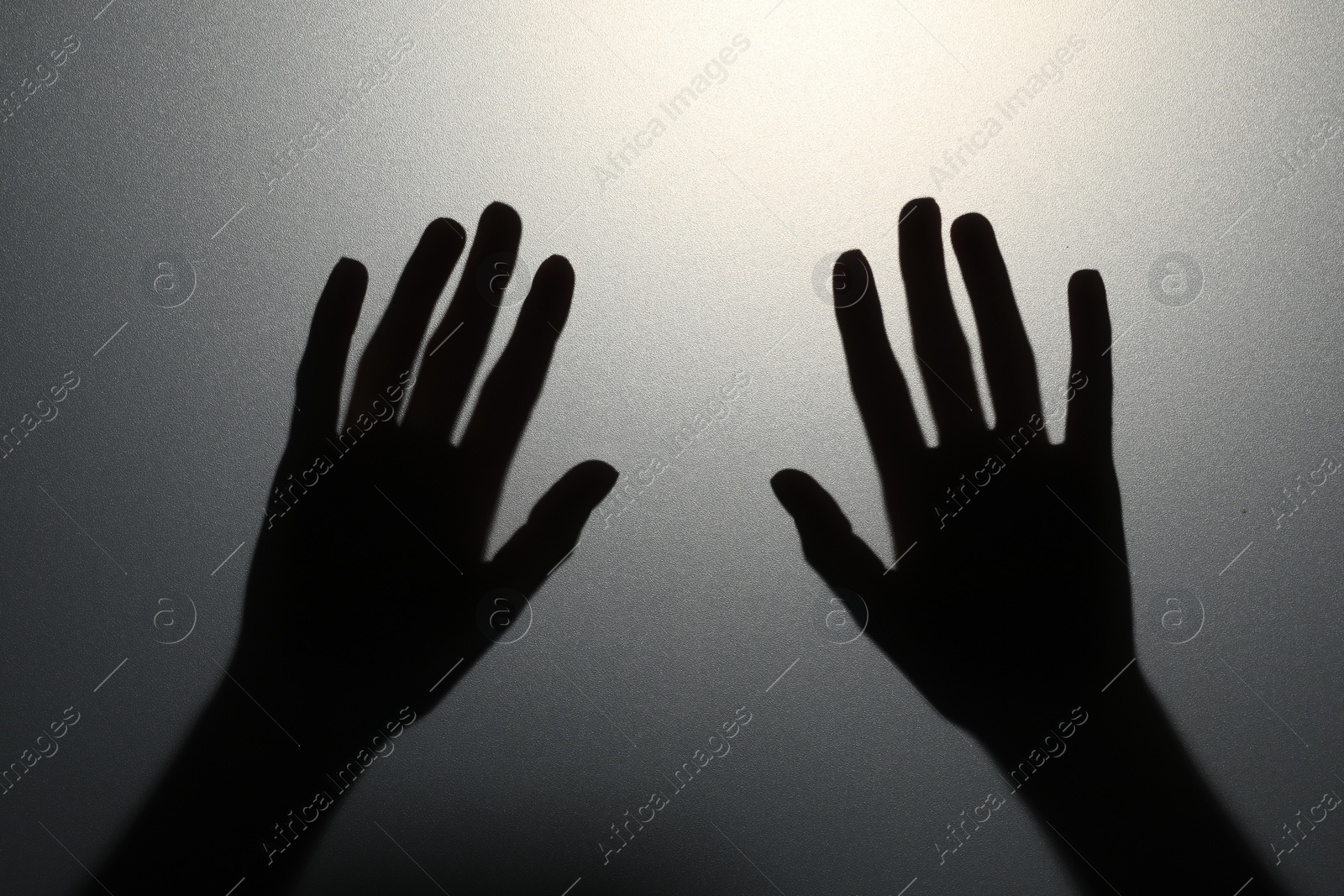 Photo of Silhouette of creepy ghost behind glass against grey background, closeup