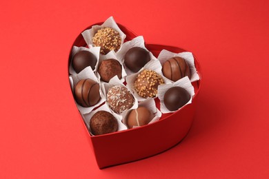 Heart shaped box with delicious chocolate candies on red table