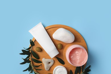 Different cosmetic products with olives and stones on light blue background, top view