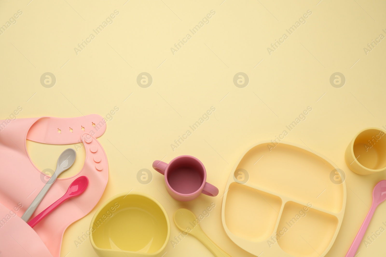 Photo of Flat lay composition with baby feeding accessories and bib on yellow background, space for text