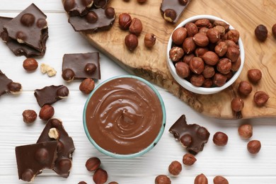 Photo of Bowl with tasty paste, chocolate pieces and nuts on white wooden table, flat lay