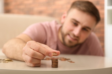 Photo of Young man with coins at home, closeup. Saving money