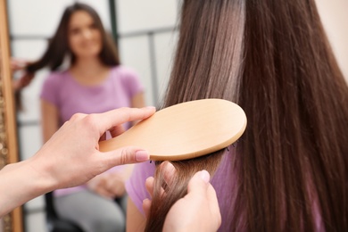 Woman combing friend's hair with cushion brush indoors, closeup