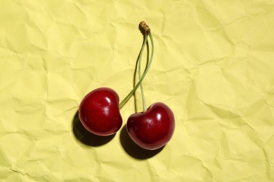 Photo of Sweet red cherries on creased yellow paper, top view