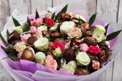 Photo of Beautiful bouquet of flowers and chocolate candies on white wooden background, closeup