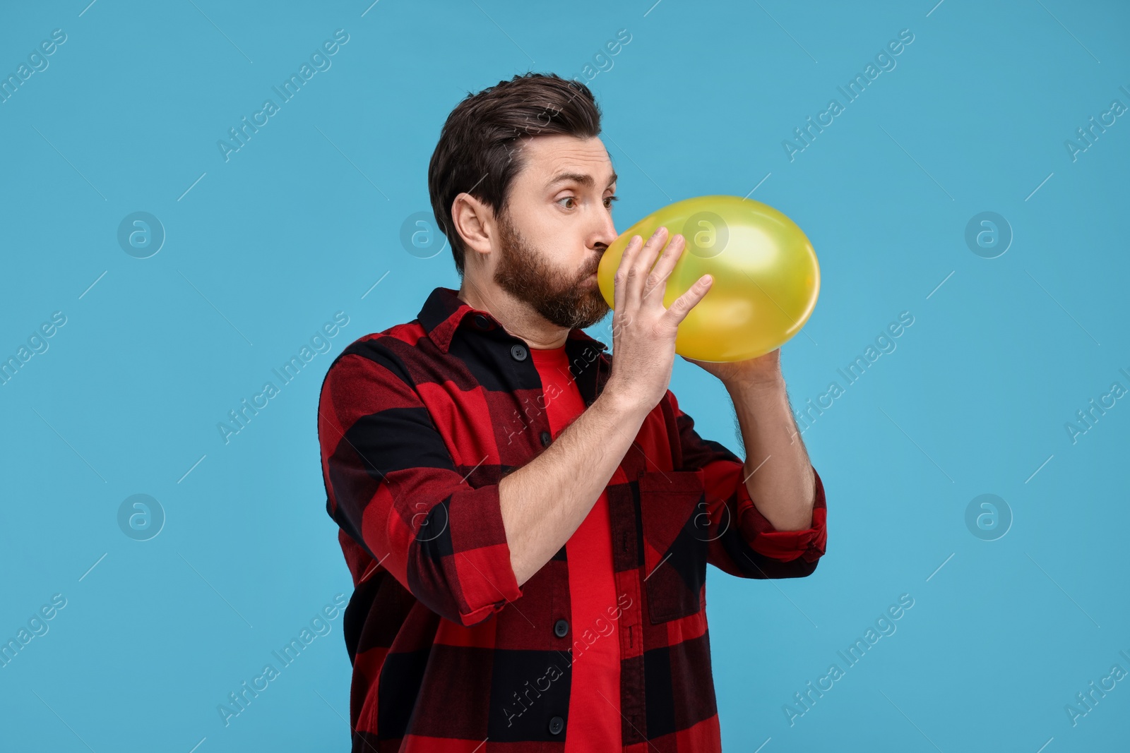 Photo of Man inflating yellow balloon on light blue background