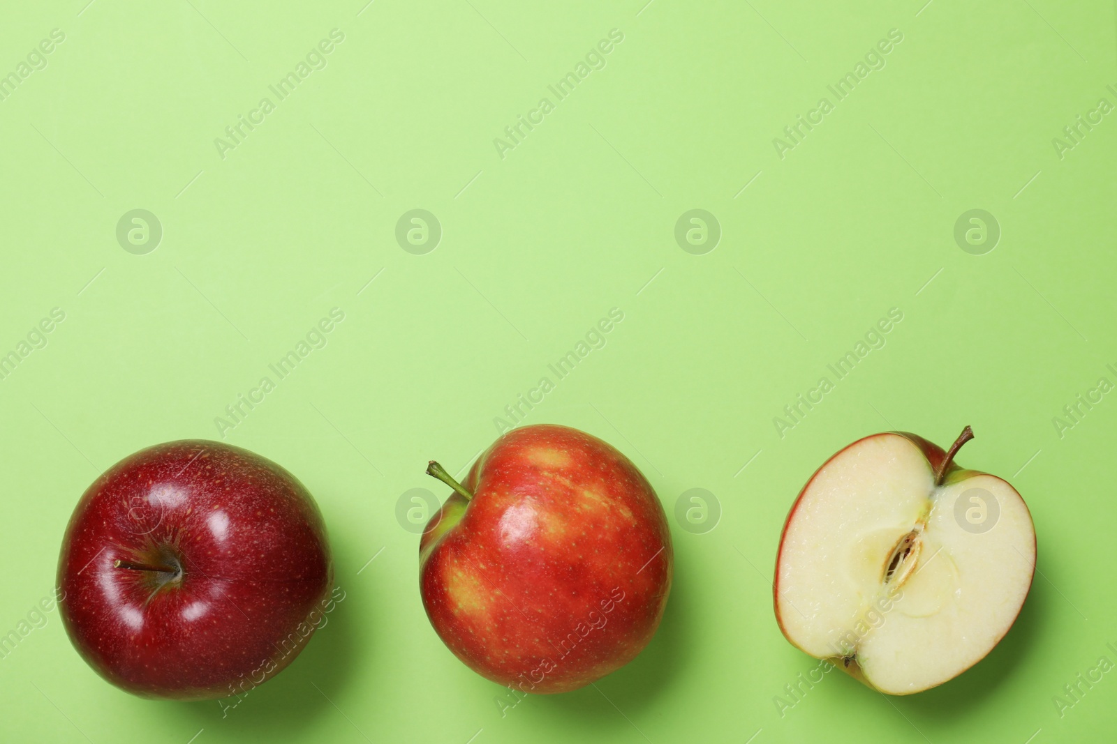 Photo of Tasty red apples on green background, flat lay. Space for text