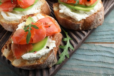 Delicious sandwiches with cream cheese, salmon, avocado and arugula on light blue wooden table, closeup