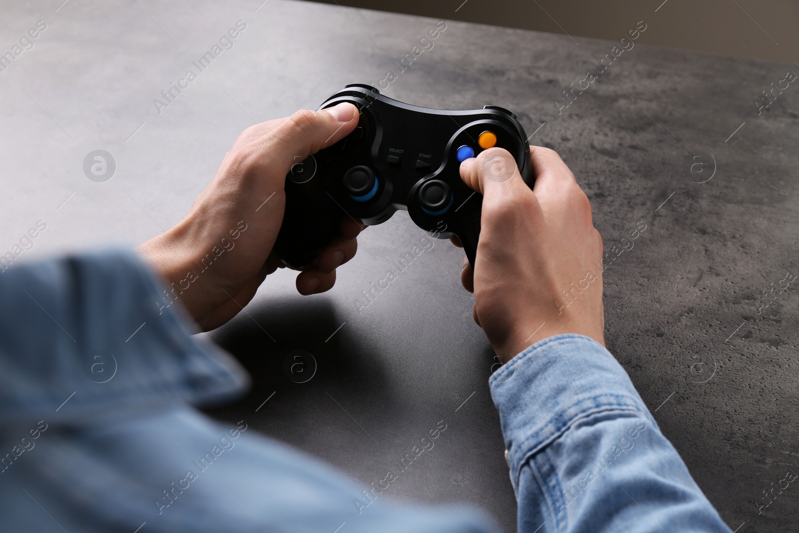 Photo of Man using wireless game controller at grey table, closeup