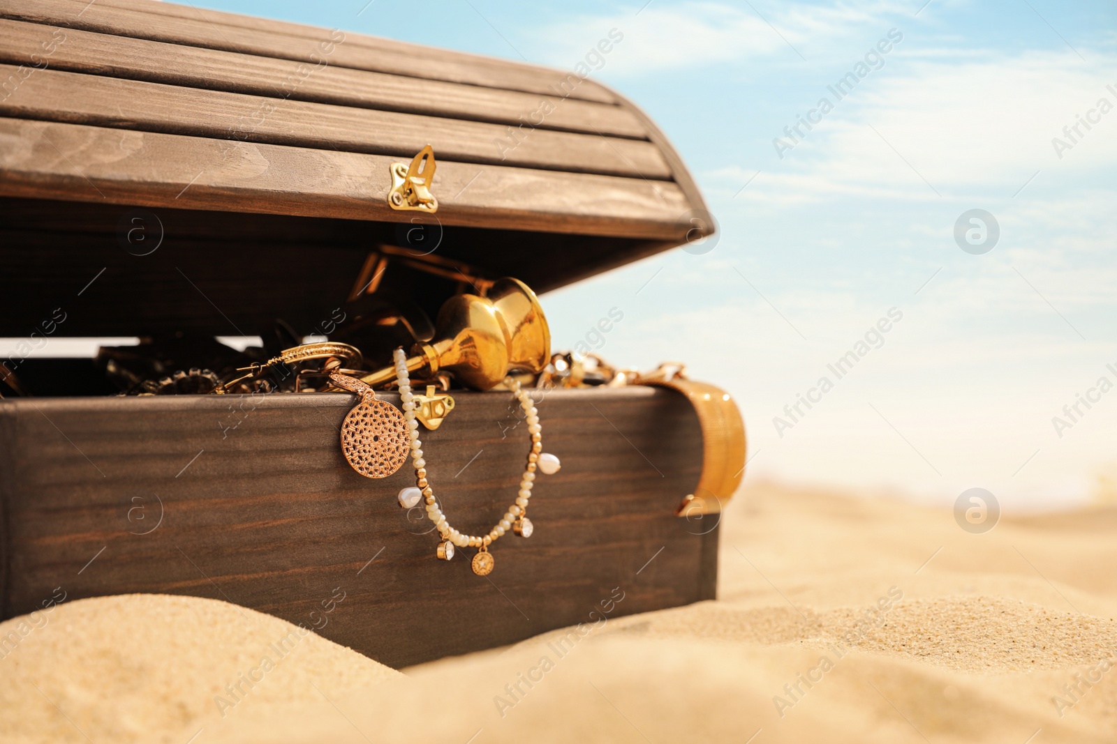 Photo of Open wooden chest with treasures on sandy beach, space for text