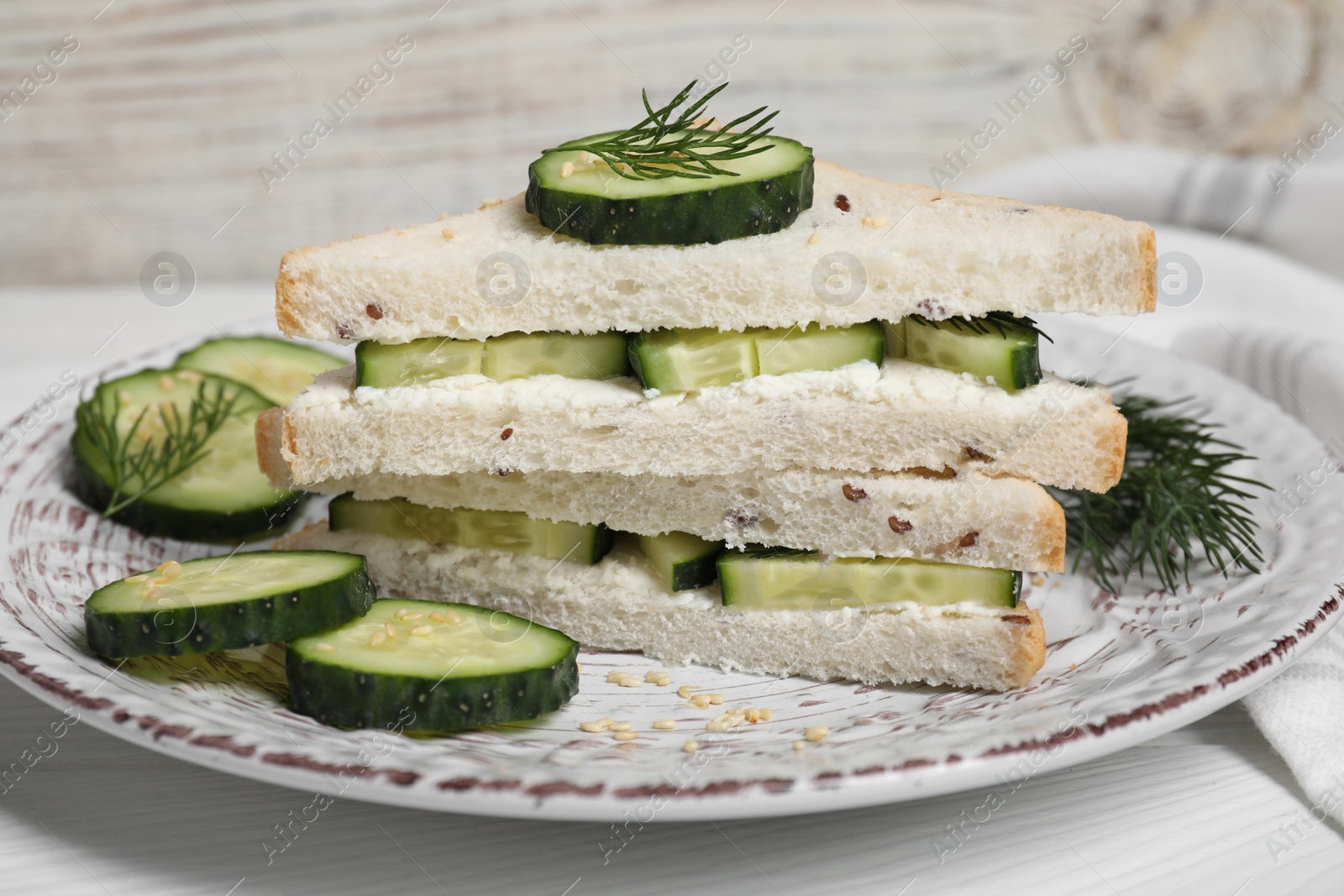 Photo of Tasty cucumber sandwiches with sesame seeds and dill on white wooden table, closeup
