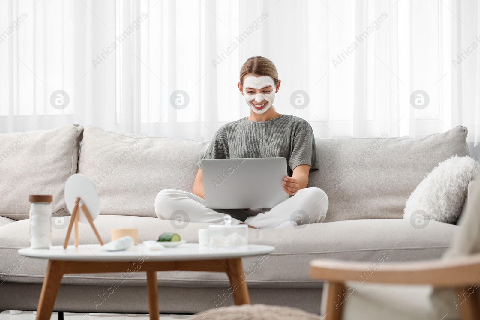 Photo of Young woman with face mask using laptop on sofa at home. Spa treatments